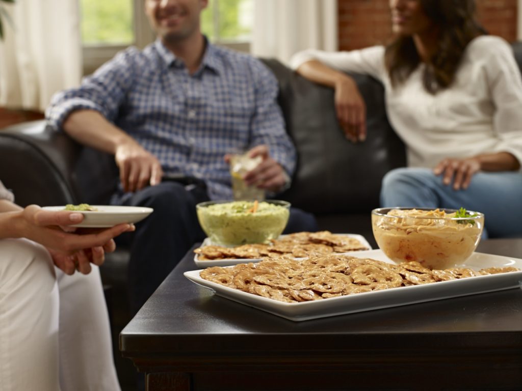 people eating pretzel crisps and dip around a couch